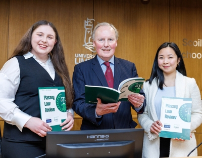 Two women and a man wearin suits smiling for a photo holding copies of the Plassey Law Review