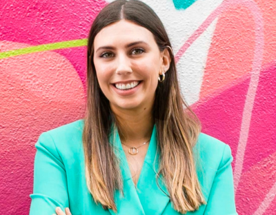 A woman in a bright green suit jacket standing against a wall with a pink mural