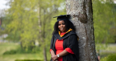 Student in graduation gown leaning against tree
