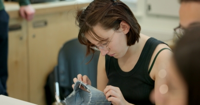 A photo of a student in UL's Makerspace learning how to mend clothes sustainably. The student is holding a piece of material and examining the repair work done.