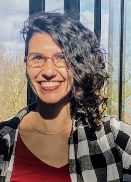 A woman with dark curly hair and glasses smiling