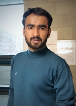 A man with dark hair and a beard smiling wearing a dark blue polo neck shirt