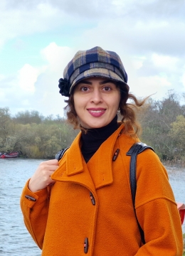 A woman outside by a lake wearing a hat and orange coat