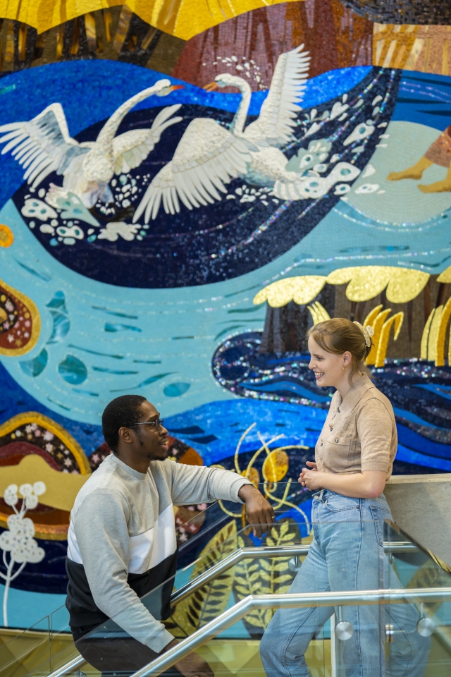 two students standing on stairs in front of a mural