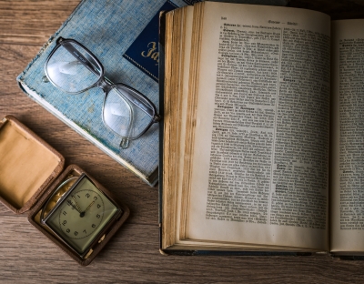 Image shows book on a table with some glasses and a watch