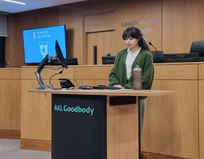 A student speaking at the podium of UL's moot courtroom. The graphic of UN SDG 6: Clean Water and Sanitation is on a digital monitor in the background.