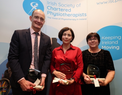 Professor Kieran  O'Sullivan, Dr Brona Fullen and Cinny Cusack holding awards at an event for the irish society of chartered physiotherapists, standing in front of a banner.