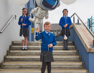 Three children in school uniforms standing on steps with space ballons 