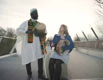 Man playing bongos and woman playing bodran, a traditional Irish instrument, on U.L's Living Bridge