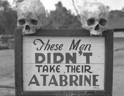 Two skulls sitting on either side of a sign that reads "These Men Didn't Take Their Atabrine".