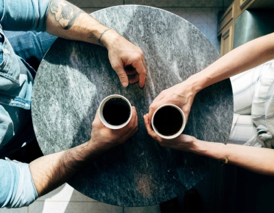Aerial view of man and woman holding coffee cups on a circular café style table.
