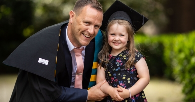 a postgraduate student poses with his daughter on graduation day. They are both smiling, the child in the photo is wearing her father's graduation cap.