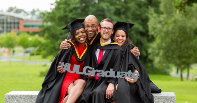 four UL students in graduation robes posing for a photo holding a #ULgraduate prop