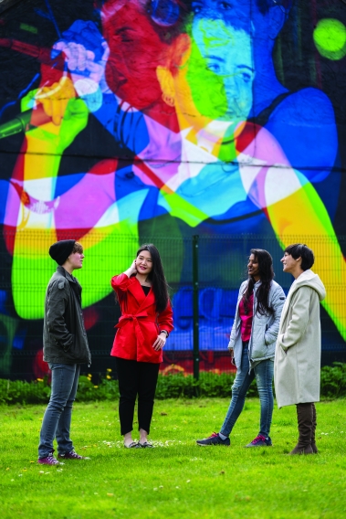 four students standing in front of wall mural