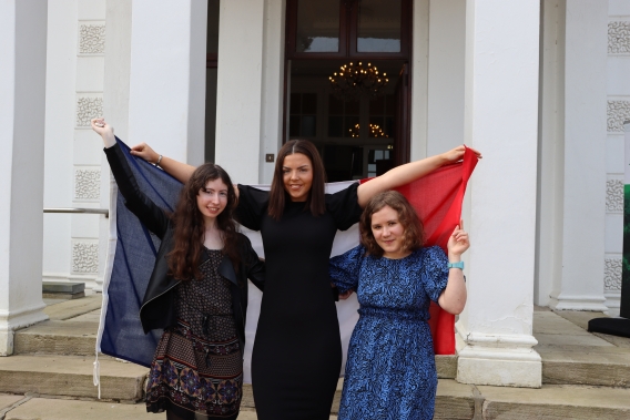3 women hold a french flag behind them in front of Plassey House