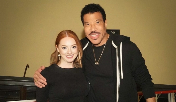 A woman wearing black top and pants with red hair posing with performer Lionel Richie 
