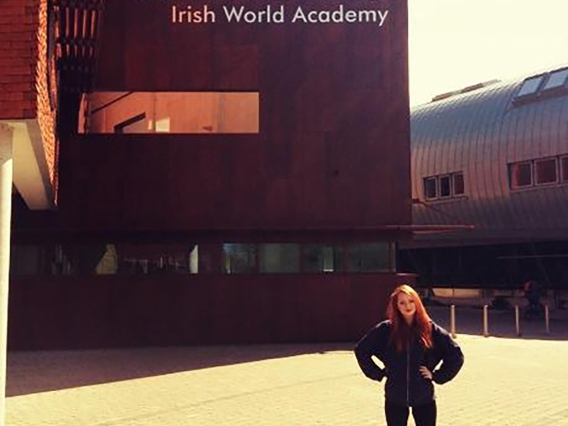 A woman with red hair wearing all back standing in front of the Irish World Academy building in University of Limerick