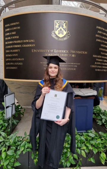 anna kurochkina, llm international commercial law, on graduation day holding her parchment beside the UL Logo