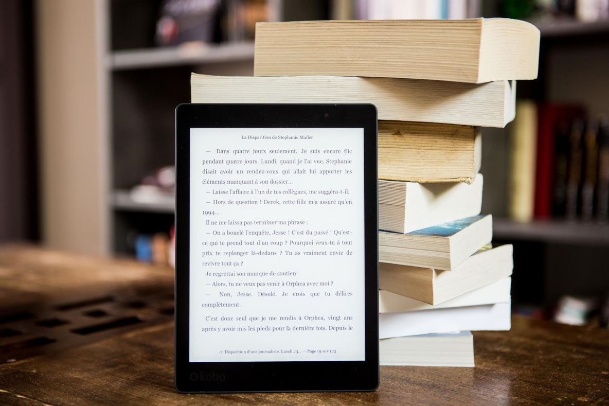 Tablet in front of pile of books laying on a wooden table