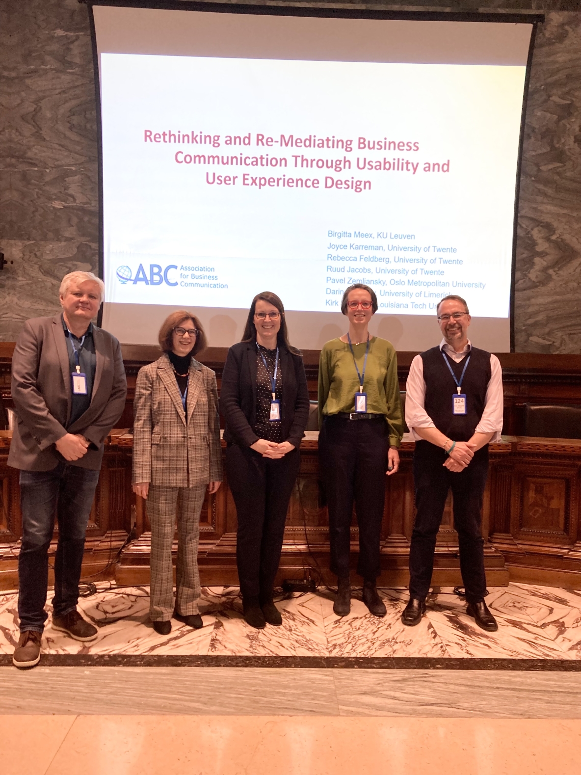 Panel presenters Pavel Zemliansky, Birgitta Meex, Darina Slattery, Joyce Karreman, and Kirk St.Amant smiling for a photo in front of a PowerPoint slide.