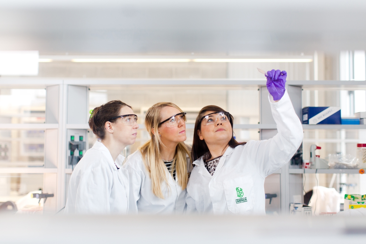 three women in lab coats examining test tube