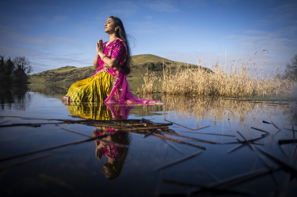 A woman sits in a lake wearing a traditional Telugu outfit consisting of a  pink voni and yellow lehenga, symbolising  happiness and prosperity. 