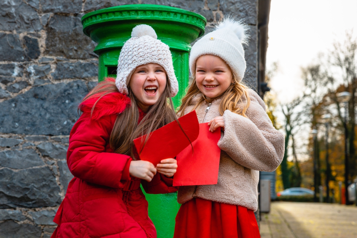 An image of two girls in front of a post box with their Santa letters