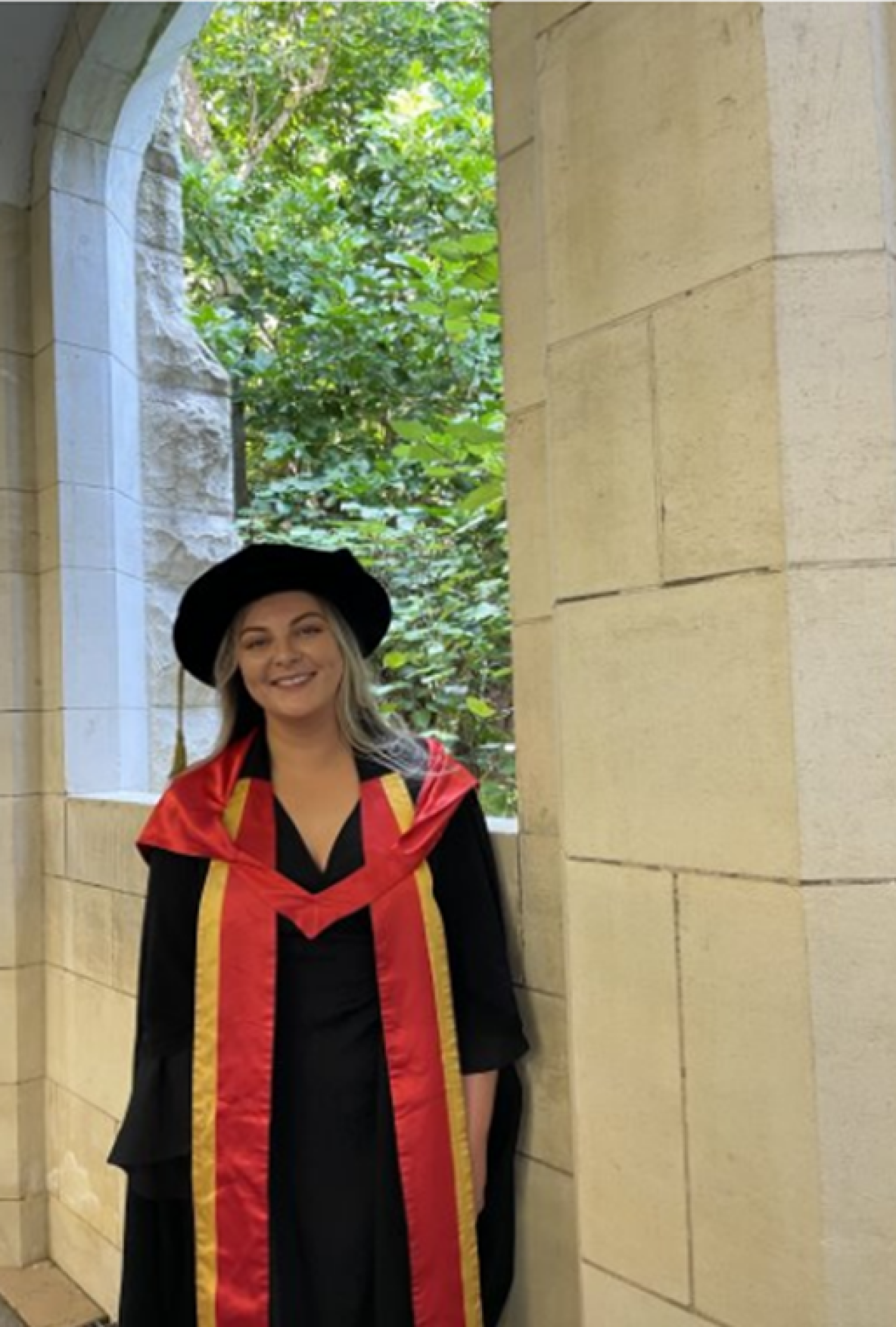 dr lynn buckley in her graduation robes and hat. she is standing in front of a stone wall.
