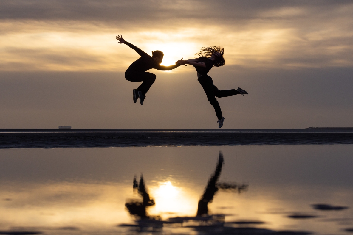 A photo of two dancers jumping against a beach background