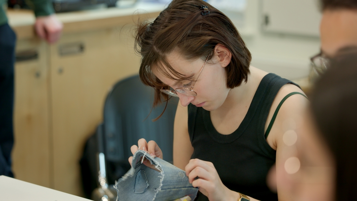 A photo of a student in UL's Makerspace learning how to mend clothes sustainably. The student is holding a piece of material and examining the repair work done.
