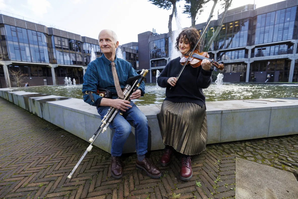 A picture of uilleann piper and musican Mickey Dunne, with his daughter Brid, seated on the fountain behind Plassey House - they are holding musical instruments