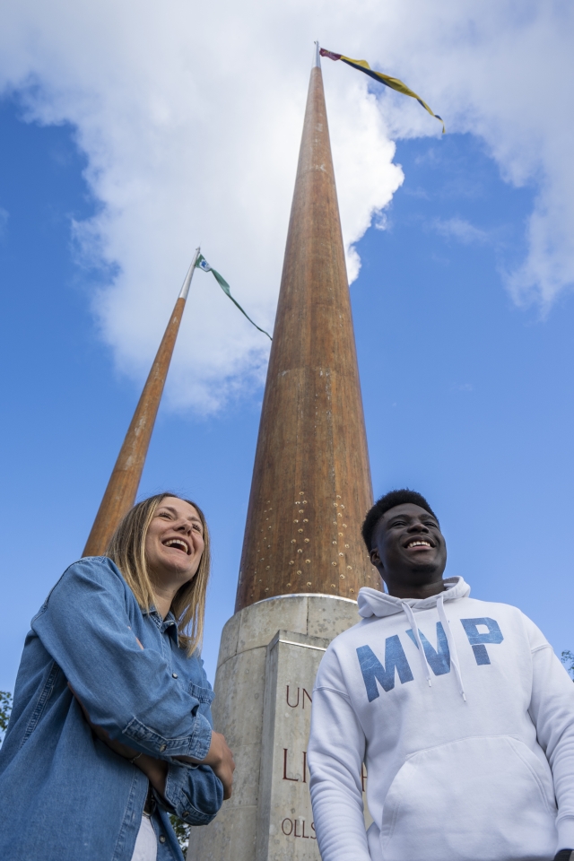 a man and woman posing and smiling under the U.L. flagpoles