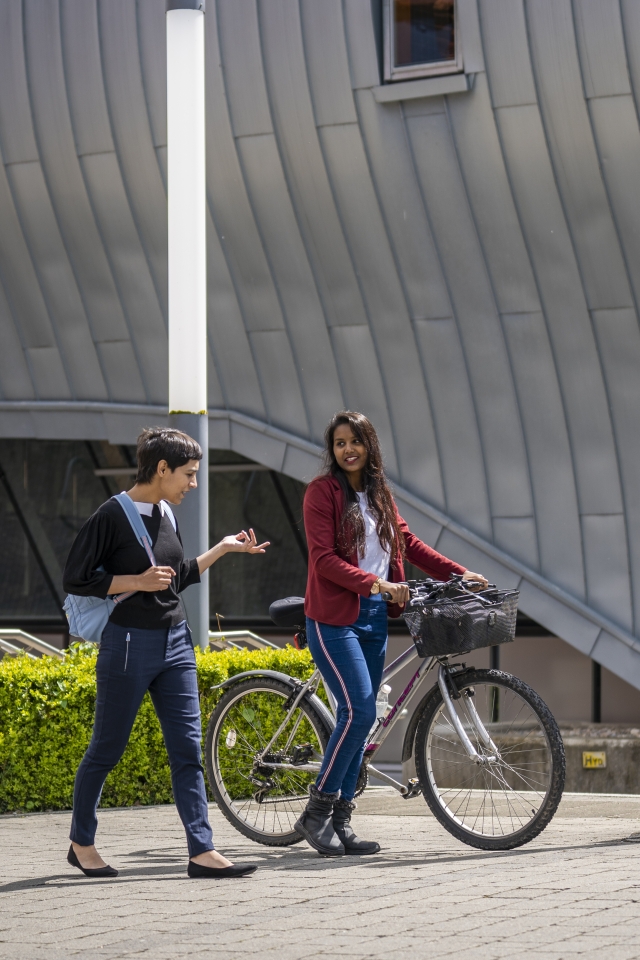two young female students talking and pushing a bicycle