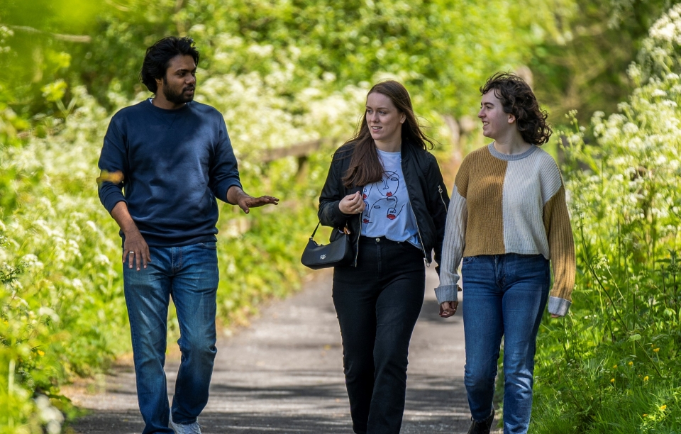 Male and two female students walking along a path, surrounded with greenery, on campus on a sunny day