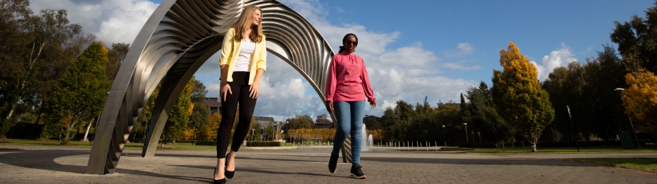 Two students walking by a metal sculpture 